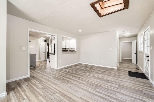 unfurnished living room with a skylight, baseboards, and light wood finished floors