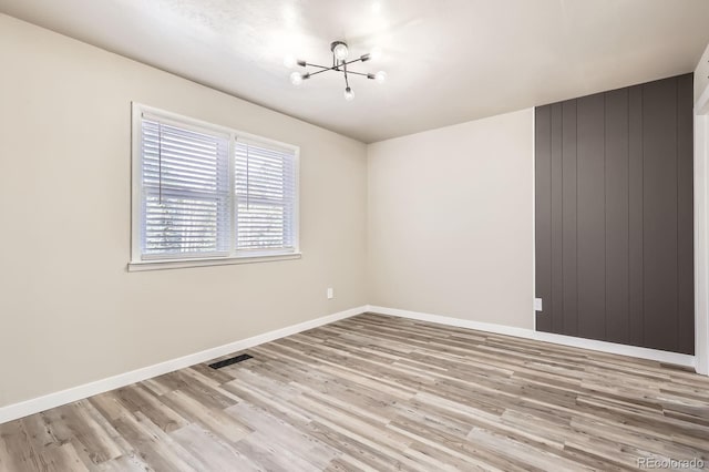 unfurnished room with baseboards, a notable chandelier, wood finished floors, and visible vents