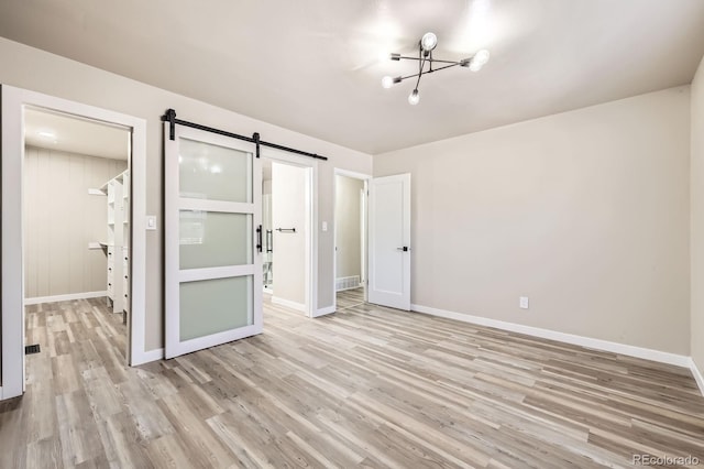 unfurnished bedroom featuring an inviting chandelier, baseboards, light wood-style floors, and a barn door