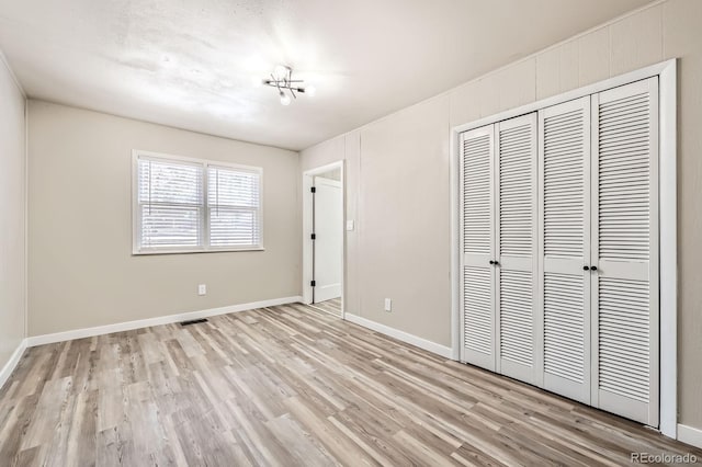 unfurnished bedroom with baseboards, a closet, light wood-style flooring, and visible vents