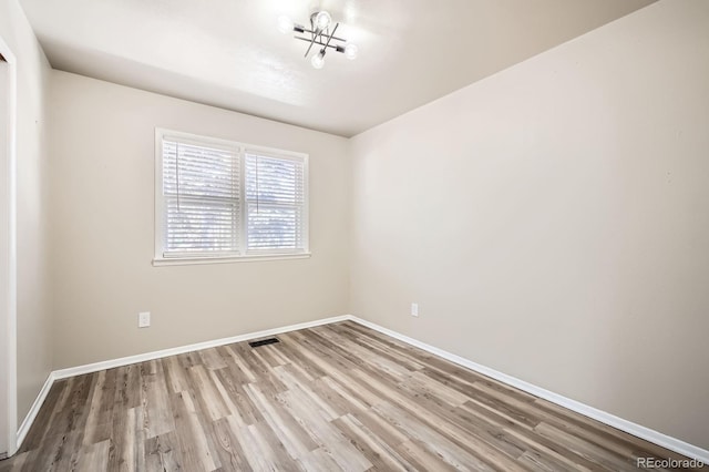 spare room featuring baseboards, a notable chandelier, wood finished floors, and visible vents
