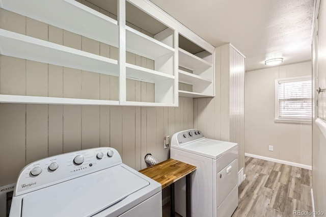 laundry area featuring laundry area, baseboards, wooden walls, light wood-type flooring, and washing machine and clothes dryer