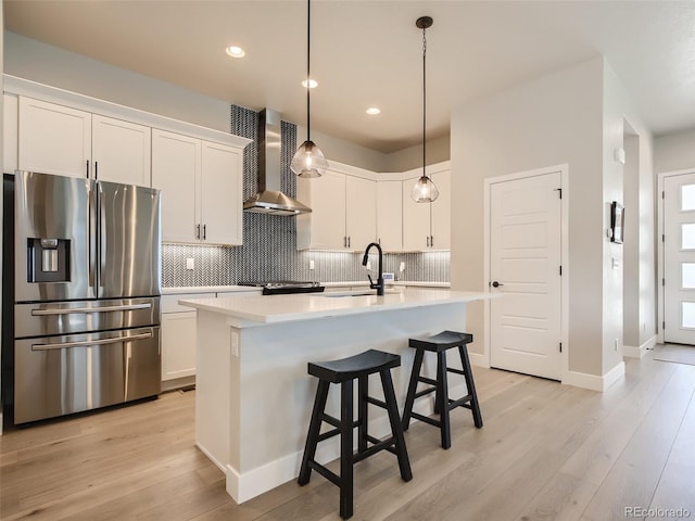 kitchen featuring an island with sink, light wood-type flooring, wall chimney exhaust hood, and stainless steel appliances