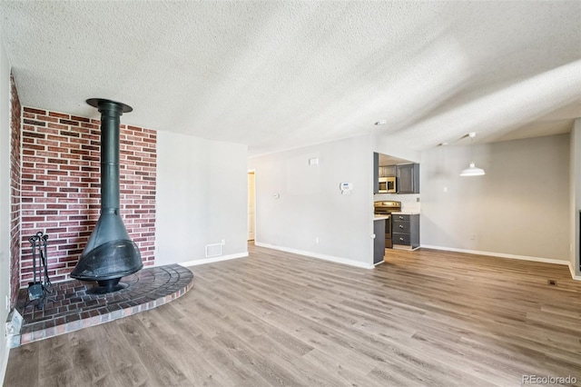 14590 E 13th Ave, Aurora, CO 80011 - unfurnished living room featuring a textured ceiling, light wood-style floors, and a wood stove