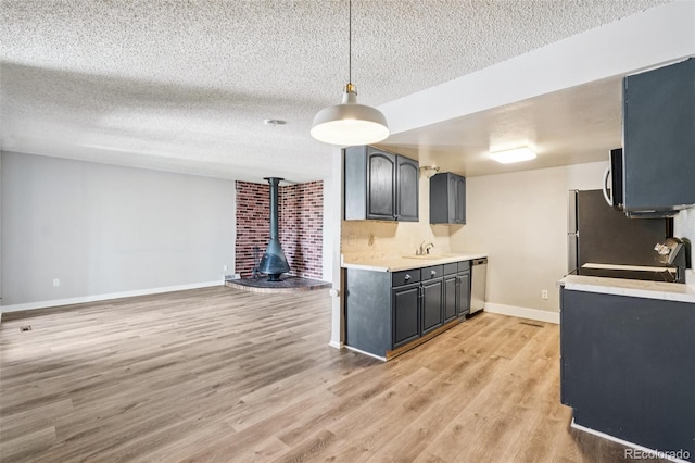 14590 E 13th Ave, Aurora, CO 80011 - kitchen featuring a textured ceiling, appliances with stainless steel finishes, light countertops, light wood-style floors, and a wood stove