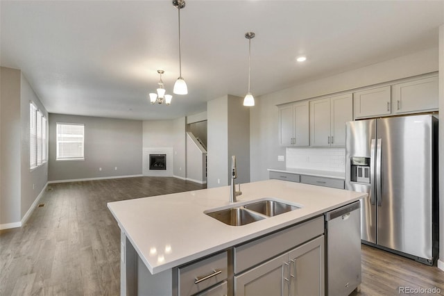 kitchen with gray cabinets, appliances with stainless steel finishes, an island with sink, sink, and backsplash