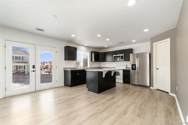 kitchen featuring a kitchen island, stainless steel appliances, dark cabinetry, light wood-style floors, and recessed lighting