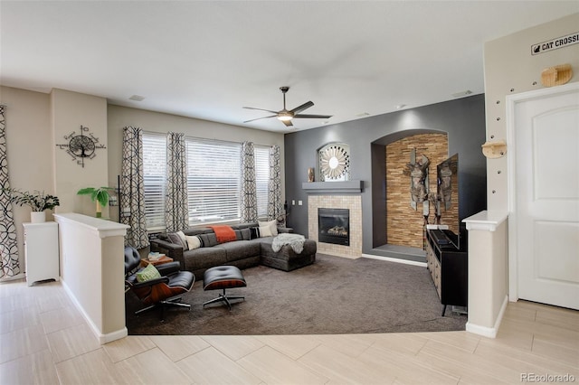 living area with a tile fireplace, baseboards, a ceiling fan, and arched walkways
