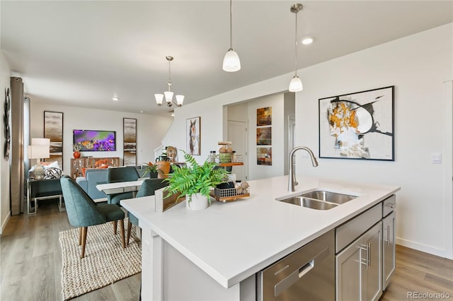 kitchen with dishwasher, an island with sink, sink, hanging light fixtures, and dark wood-type flooring