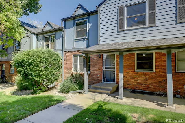 property entrance featuring roof with shingles and brick siding