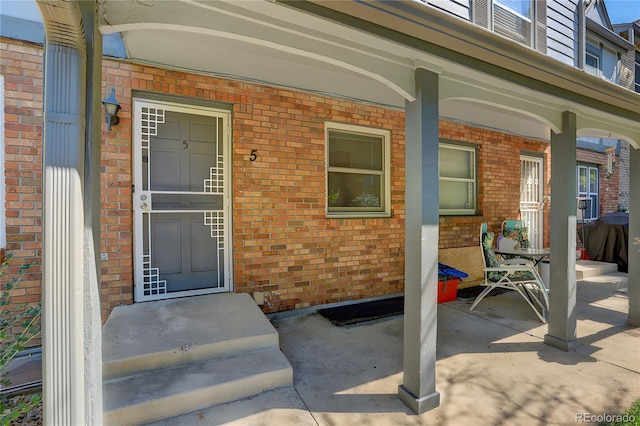 view of exterior entry with a porch and brick siding