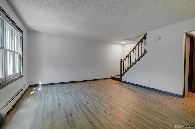 unfurnished room with baseboards, wood finished floors, stairs, a textured ceiling, and a baseboard heating unit