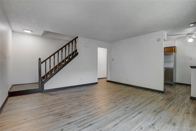 unfurnished living room with a textured ceiling, a ceiling fan, baseboards, stairs, and light wood-style floors