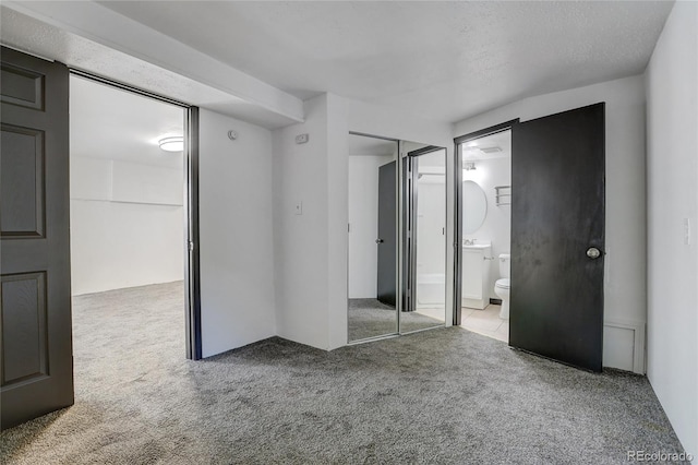 unfurnished bedroom with carpet, a closet, connected bathroom, and a textured ceiling