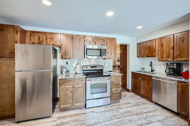 kitchen with appliances with stainless steel finishes, light stone countertops, sink, and decorative backsplash