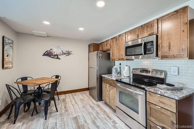 kitchen with appliances with stainless steel finishes, light stone countertops, decorative backsplash, and light wood-type flooring