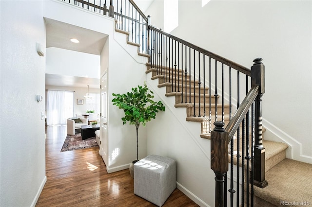 stairway featuring a high ceiling, baseboards, and wood finished floors