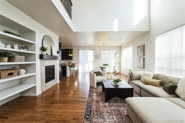 living area featuring built in shelves, dark wood-type flooring, a towering ceiling, and a tile fireplace