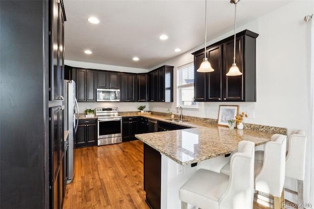 kitchen featuring a sink, light stone counters, appliances with stainless steel finishes, a peninsula, and dark wood-style flooring