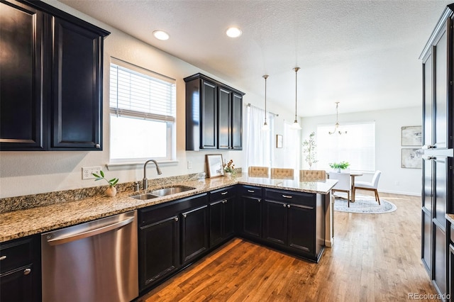 kitchen featuring dark wood finished floors, dark cabinets, a peninsula, stainless steel dishwasher, and a sink