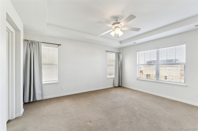 carpeted empty room featuring baseboards, a raised ceiling, and ceiling fan