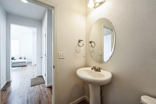 bathroom featuring visible vents, toilet, wood finished floors, baseboards, and a textured wall