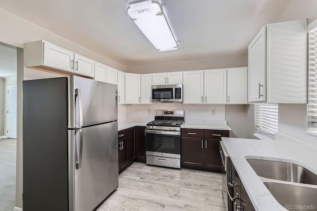 kitchen with sink, appliances with stainless steel finishes, dark brown cabinetry, white cabinets, and light wood-type flooring