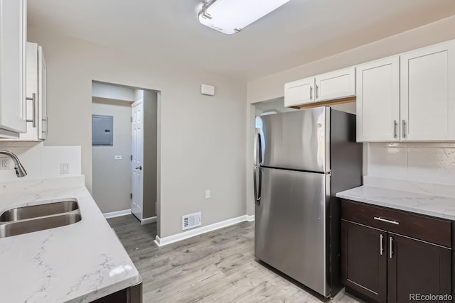 kitchen featuring a sink, electric panel, backsplash, white cabinetry, and freestanding refrigerator