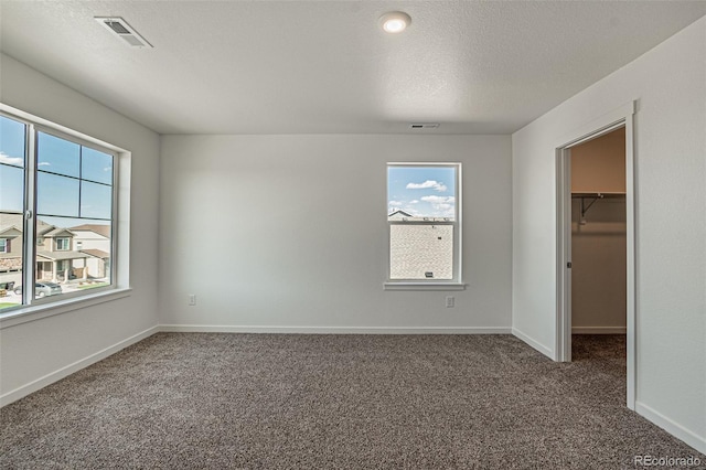 unfurnished bedroom with a textured ceiling, carpet, a walk in closet, and a closet