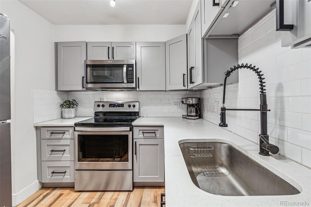 kitchen featuring stainless steel appliances, gray cabinetry, decorative backsplash, and a sink