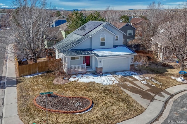 traditional-style home featuring a porch, a garage, solar panels, fence, and concrete driveway