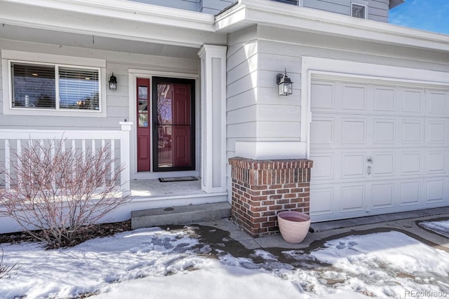 snow covered property entrance with an attached garage