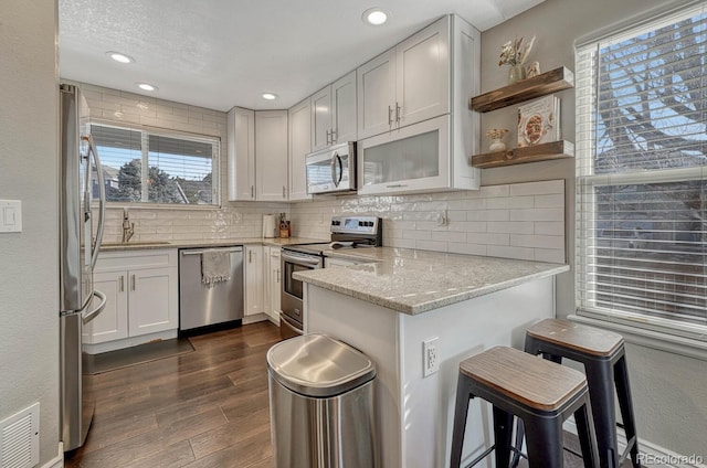 kitchen featuring appliances with stainless steel finishes, light stone counters, dark wood-type flooring, a breakfast bar area, and white cabinetry