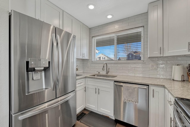 kitchen featuring light stone counters, a sink, stainless steel appliances, white cabinetry, and backsplash