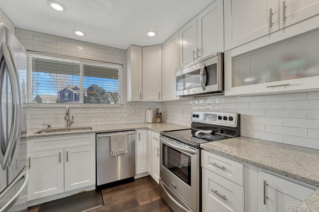 kitchen with appliances with stainless steel finishes, decorative backsplash, a sink, and white cabinets