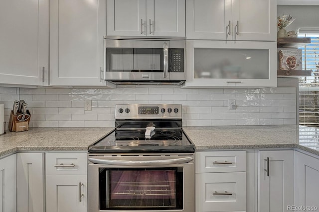 kitchen featuring light stone countertops, white cabinets, appliances with stainless steel finishes, decorative backsplash, and open shelves