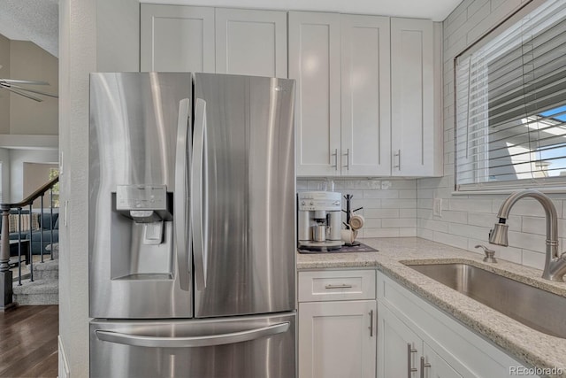 kitchen with light stone countertops, a sink, white cabinetry, stainless steel refrigerator with ice dispenser, and decorative backsplash