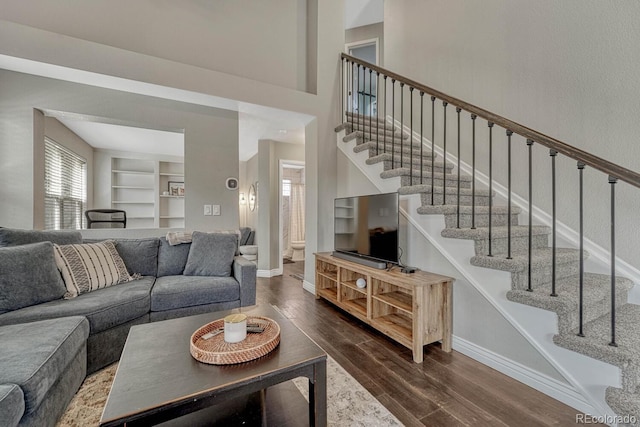 living area with dark wood-style floors, built in shelves, stairway, and baseboards