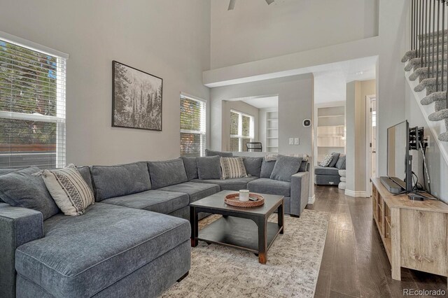 living area featuring built in features, a towering ceiling, stairway, and wood finished floors