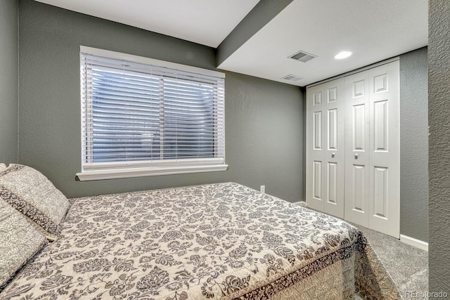 carpeted bedroom featuring a closet, visible vents, and a textured wall