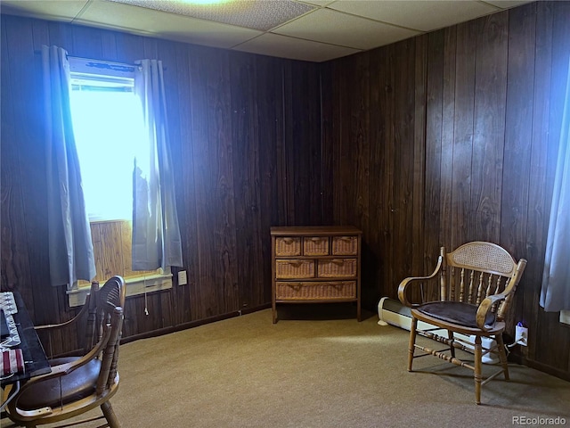 sitting room with wooden walls, light carpet, and a drop ceiling