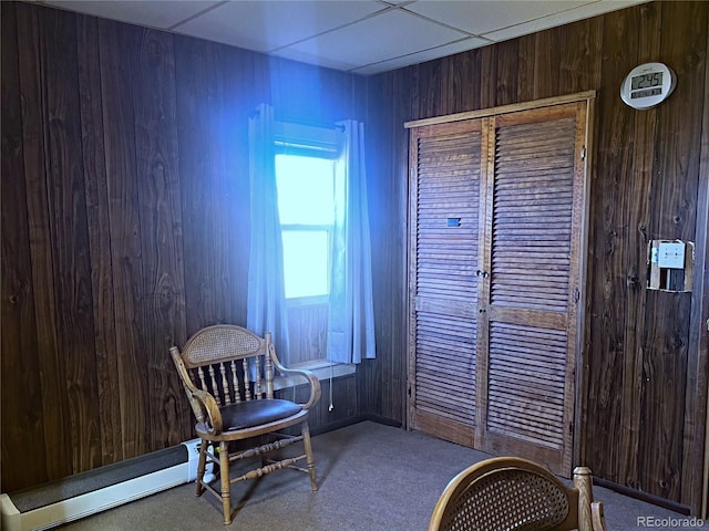 sitting room featuring carpet floors, a baseboard heating unit, wooden walls, and a drop ceiling