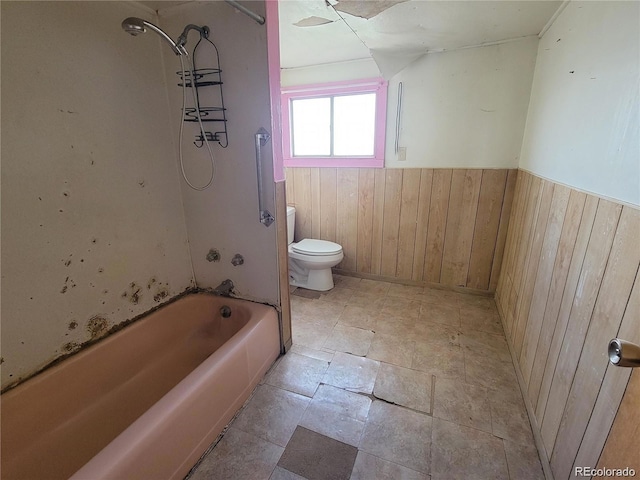 bathroom with toilet, shower / bathtub combination, and wooden walls