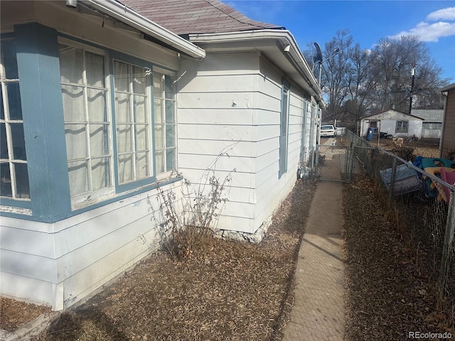 view of side of home featuring a shingled roof, fence, and a gate