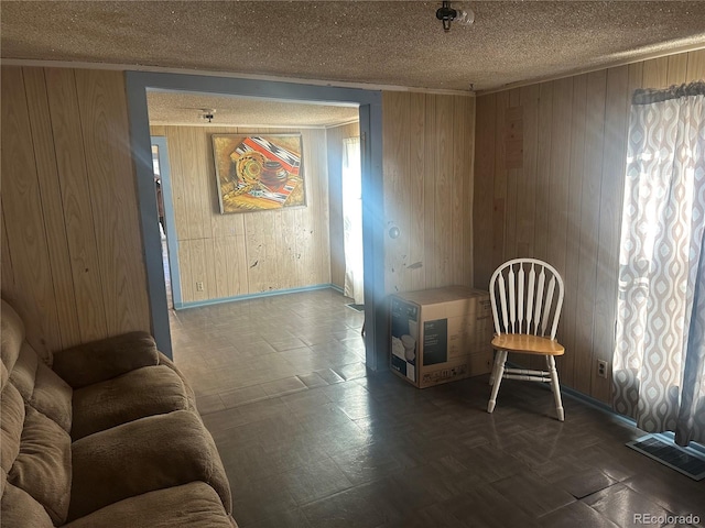 living area featuring visible vents, ornamental molding, wood walls, a textured ceiling, and tile patterned floors