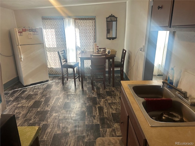 kitchen with freestanding refrigerator, a sink, and baseboards