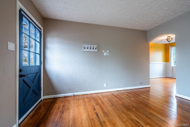 empty room with arched walkways, wood finished floors, healthy amount of natural light, a textured ceiling, and a textured wall