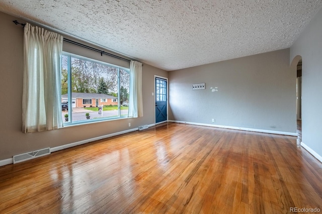 spare room with healthy amount of natural light, wood finished floors, arched walkways, a textured ceiling, and baseboards