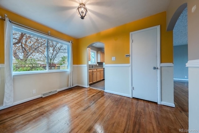 unfurnished room with arched walkways, wood finished floors, a sink, and baseboards