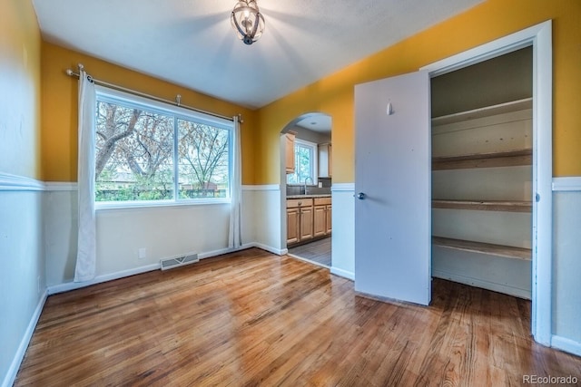 unfurnished bedroom featuring arched walkways, wood finished floors, a sink, ensuite bath, and a closet